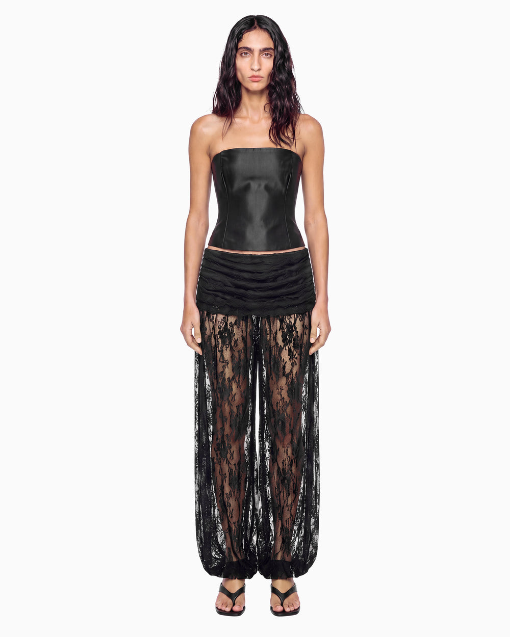 Modelo de frente com a Calça Aladim Haze preta de renda transparente, pala drapeada e top de couro tomara que caia