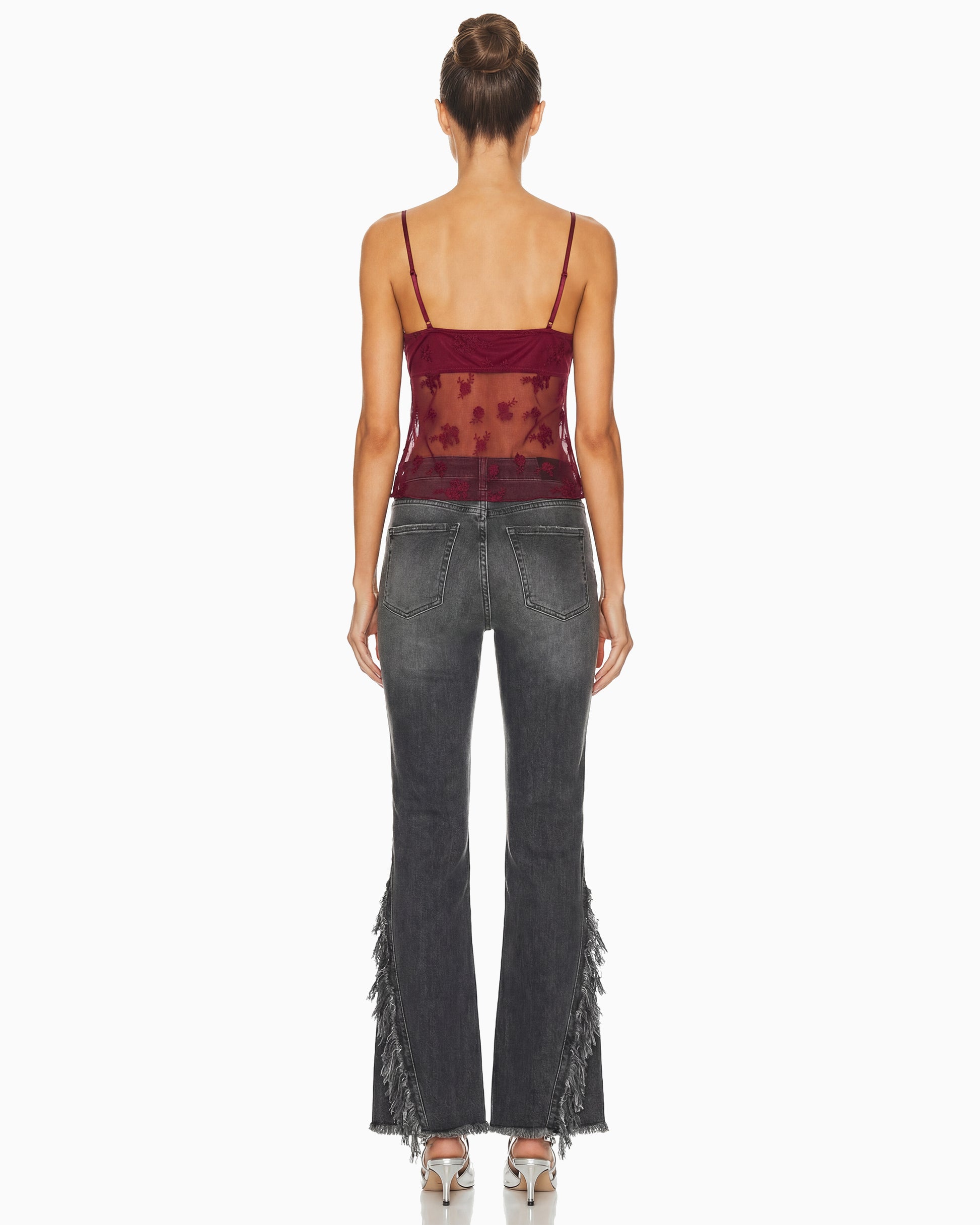Vista de costas da Calça Punk jeans cinza lavado na modelo, com bolsos traseiros, barra flare e franjas laterais
