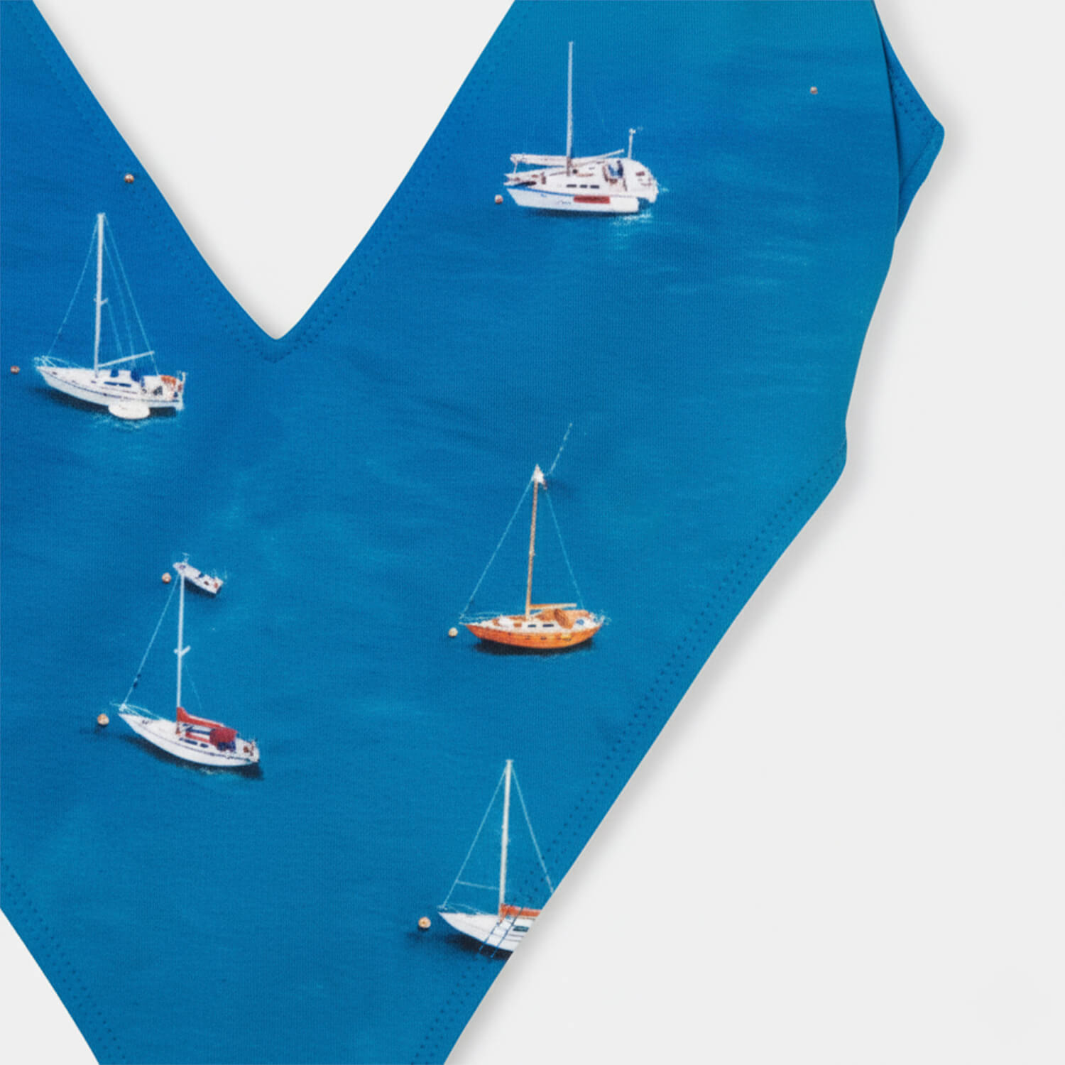 Detalhe da estampa do Maiô Barcos, veleiros brancos e laranja sobre mar azul