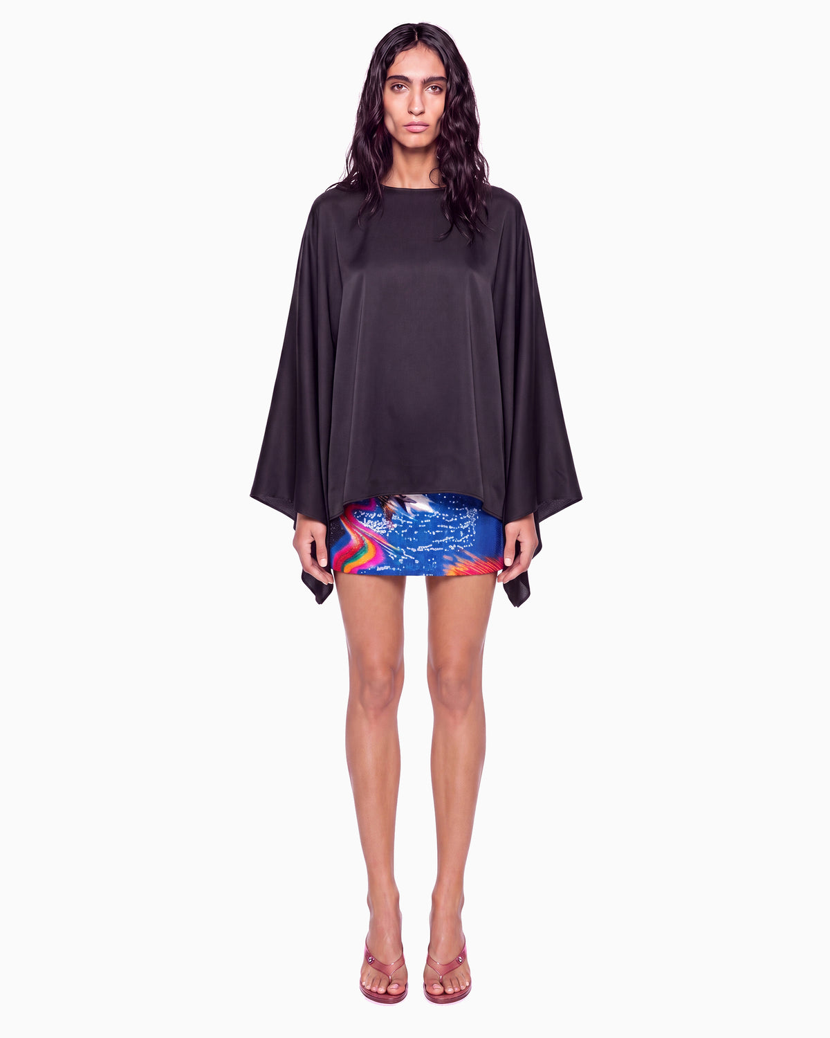 Modelo de frente com Blusa Manga Morcego Crepe Ivo preta, decote canoa e mangas amplas, com saia curta estampada