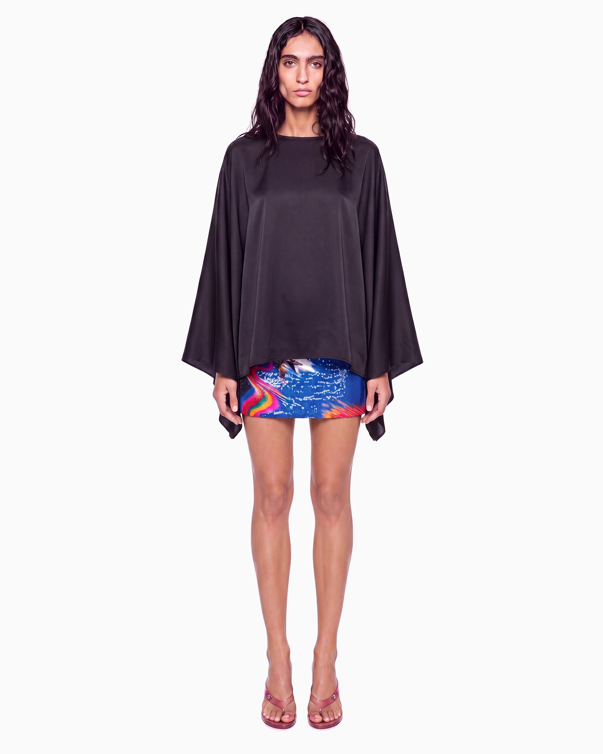 Modelo de frente com Blusa Manga Morcego Crepe Ivo preta, decote canoa e mangas amplas, com saia curta estampada