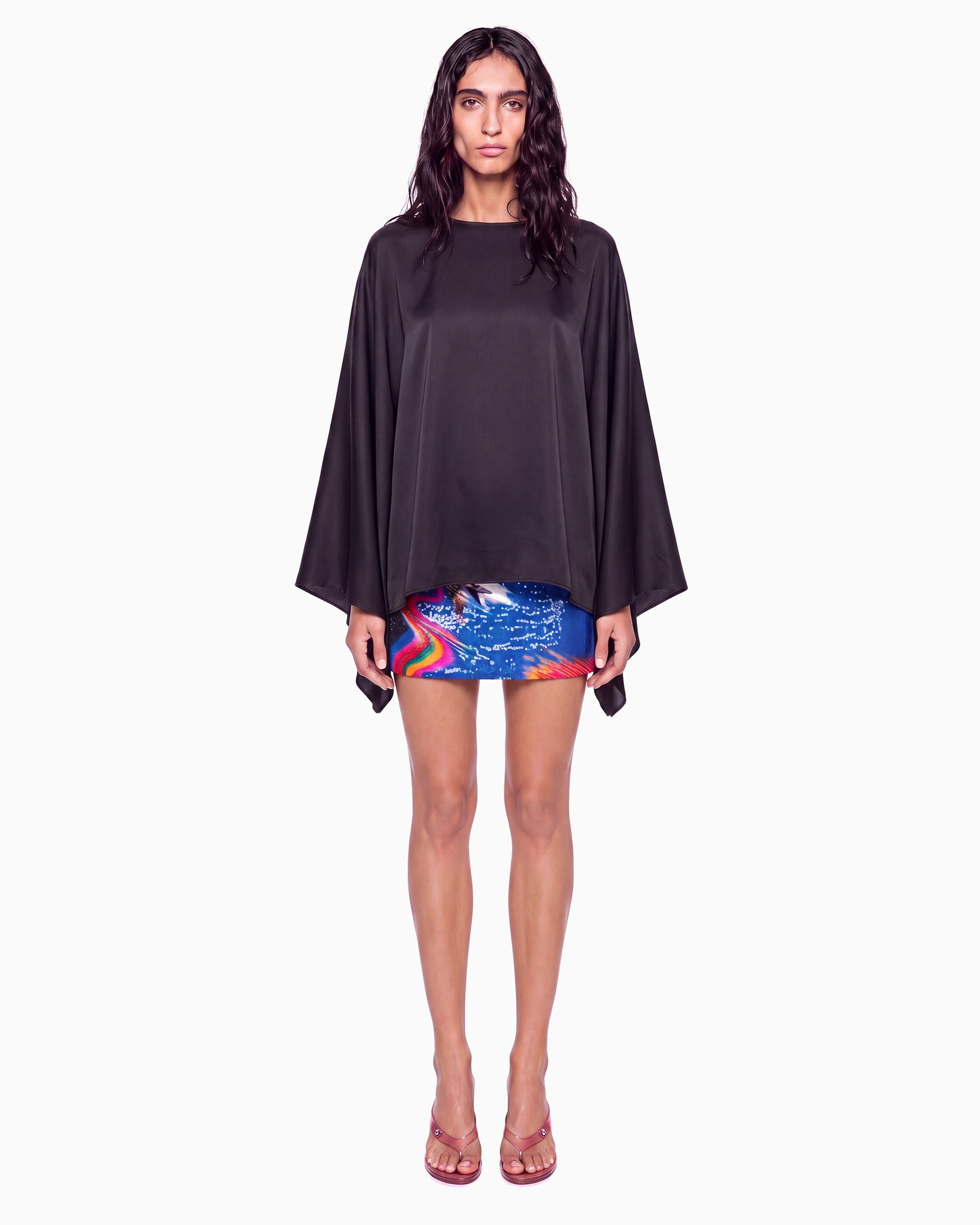 Modelo de frente com Blusa Manga Morcego Crepe Ivo preta, decote canoa e mangas amplas, com saia curta estampada