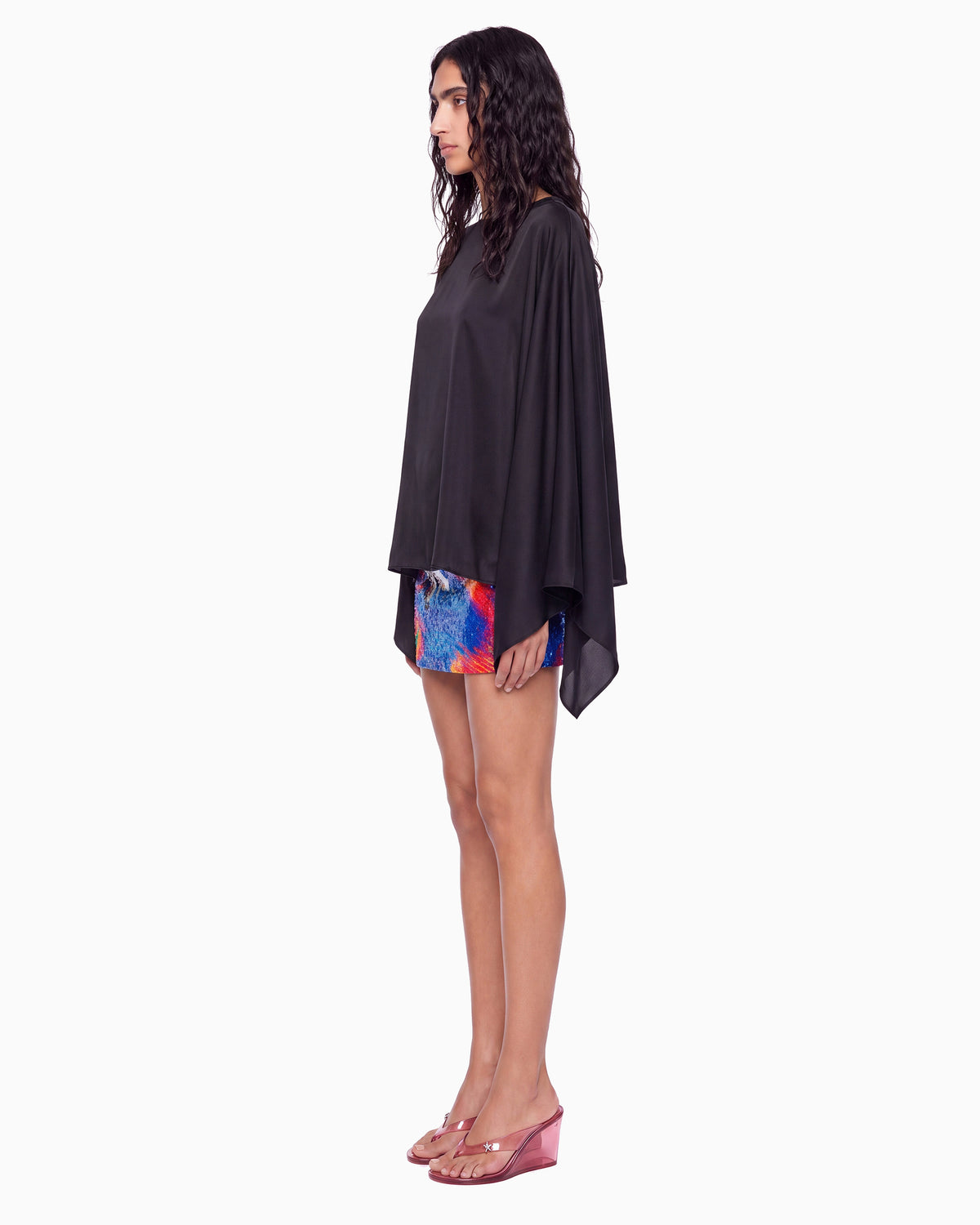 Vista lateral da Blusa Manga Morcego Crepe Ivo preta, caimento solto do cetim sobre saia curta colorida