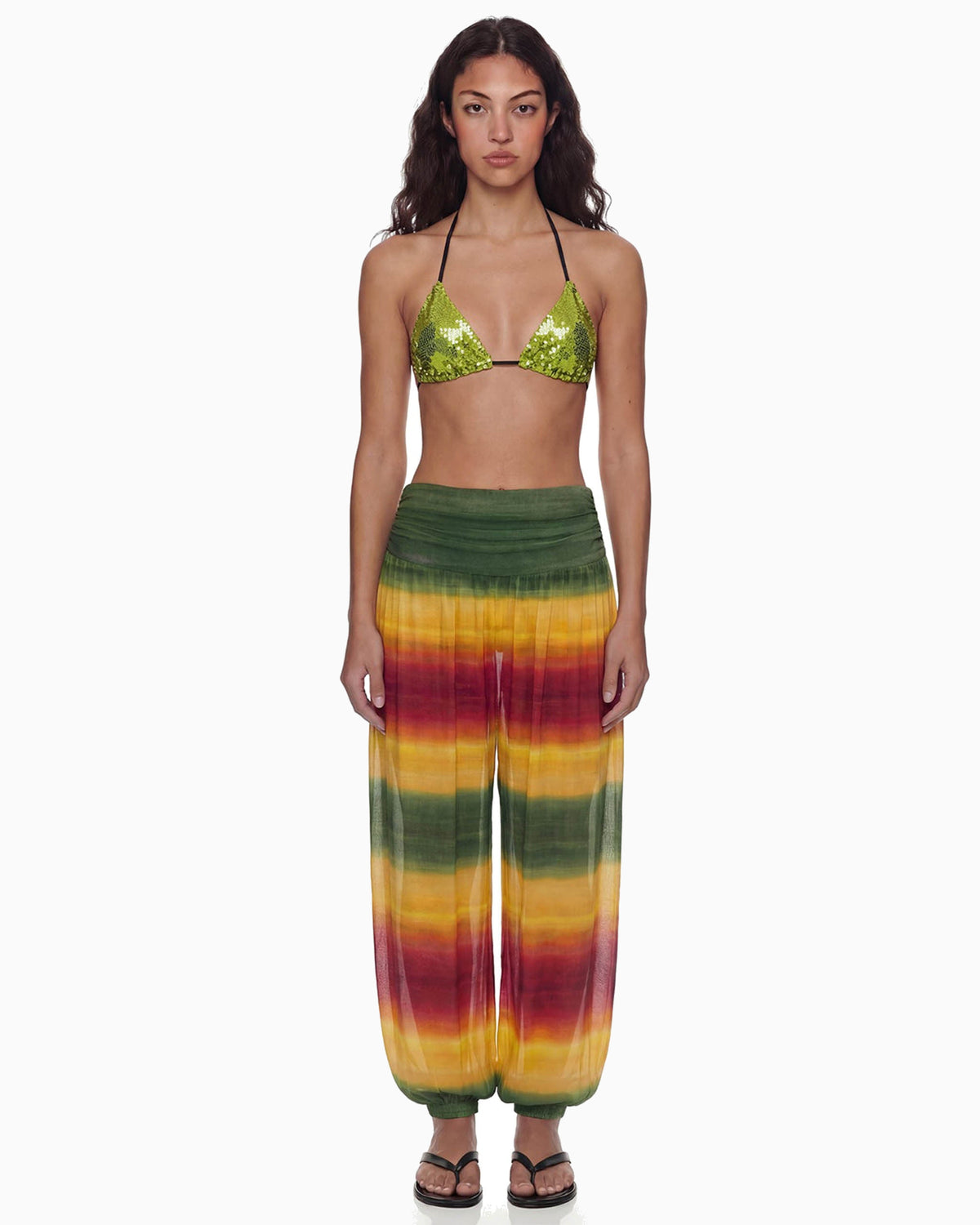 Modelo de frente vestindo a Calça Aladdin Tule Ginga em degradê verde, amarelo e vermelho, cintura alta franzida e caimento amplo