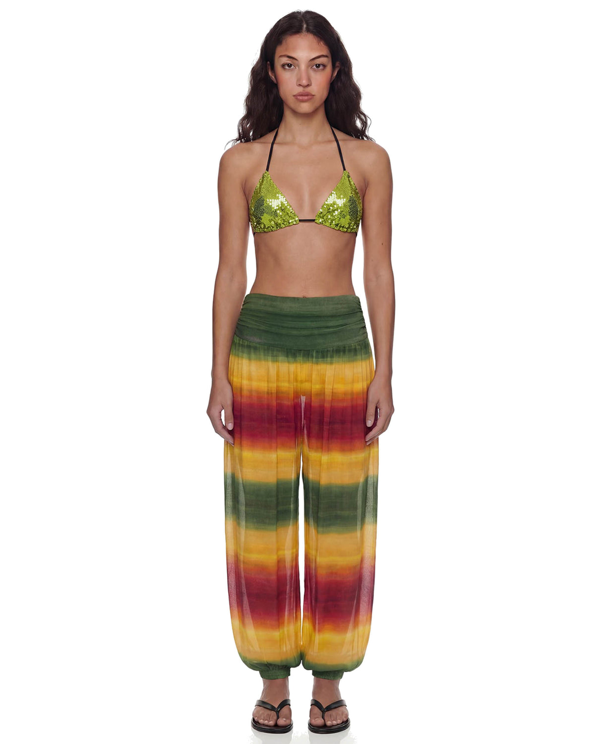 Modelo de frente vestindo a Calça Aladdin Tule Ginga em degradê verde, amarelo e vermelho, cintura alta franzida e caimento amplo