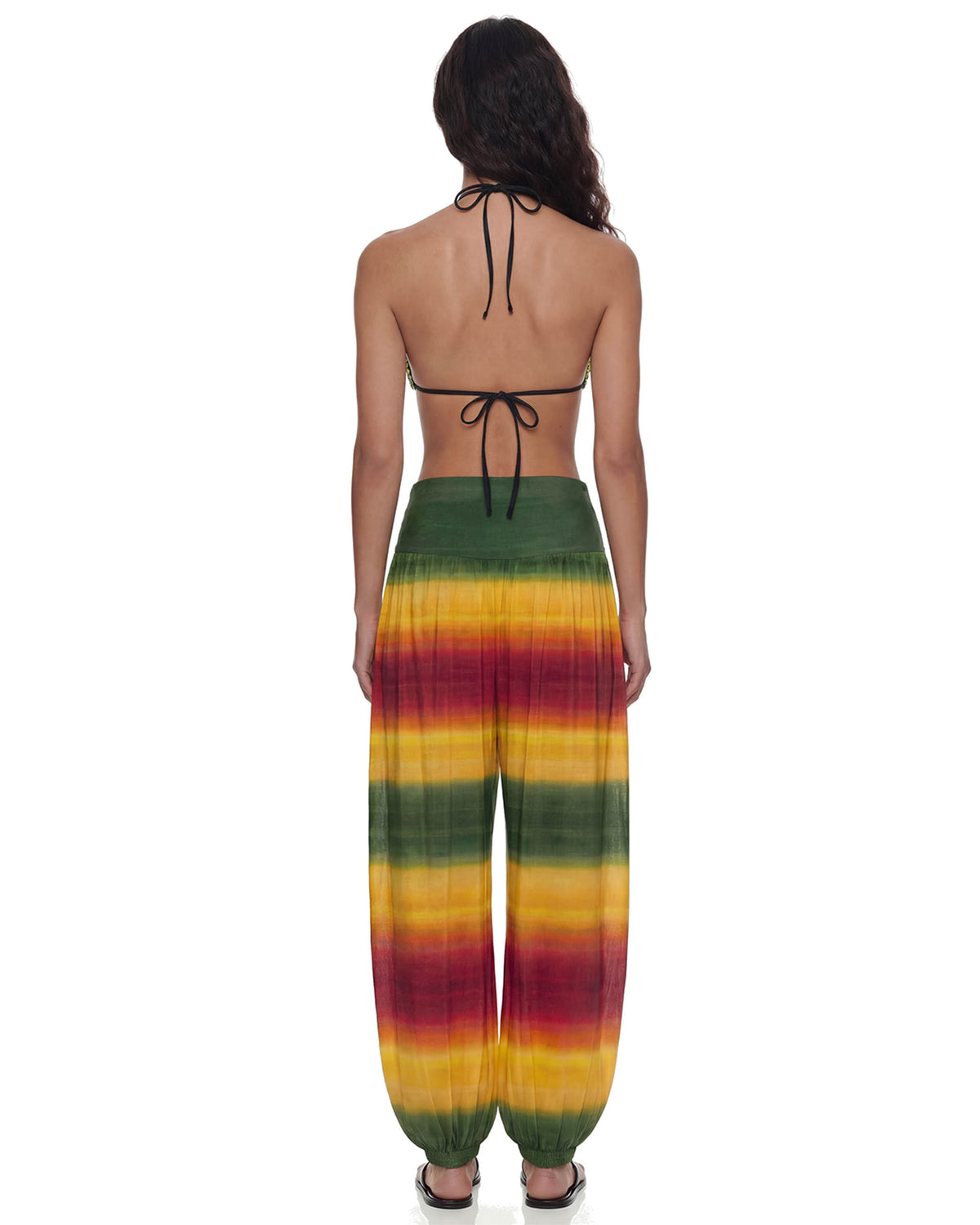 Vista de costas da Calça Aladdin Tule Ginga na modelo, degradê verde, amarelo e vermelho com caimento fluido e barra ajustada