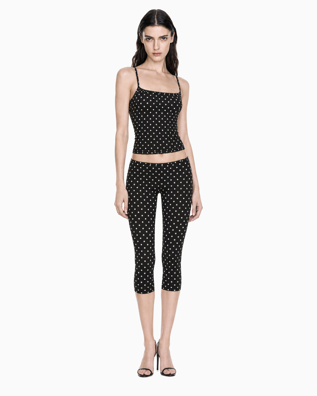 Modelo vestindo Calça Capri Cintura Baixa Poá preta com poás brancos, com regata combinando, vista frontal de corpo inteiro