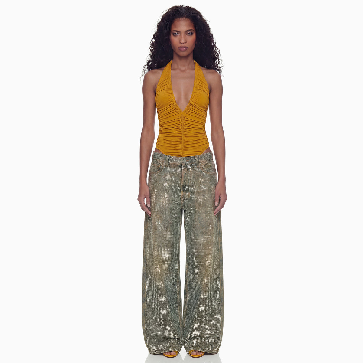 Modelo de frente com a Calça Jeans Strass pantalona brilhante e body halter mostarda, caimento largo até os pés