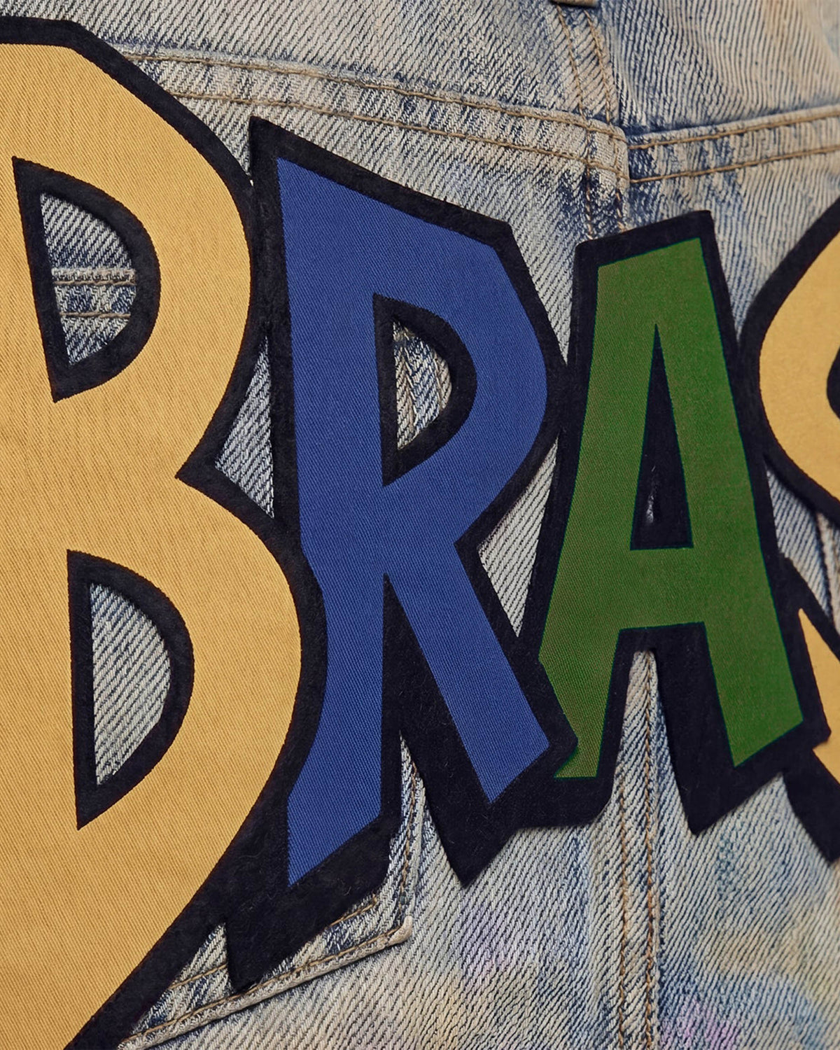 Detalhe das letras coloridas escrito Brasil na Mini Saia Jeans Brasilidades, sobre jeans claro desbotado