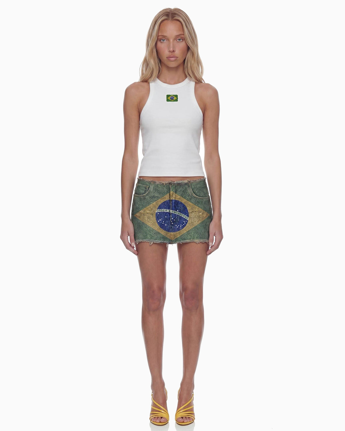 Modelo de frente com Mini Saia Strass Bandeira do Brasil e regata branca, cintura baixa e comprimento curtíssimo