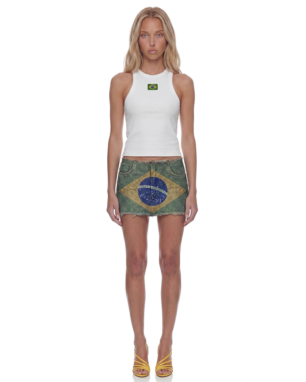 Modelo de frente com Mini Saia Strass Bandeira do Brasil e regata branca, cintura baixa e comprimento curtíssimo