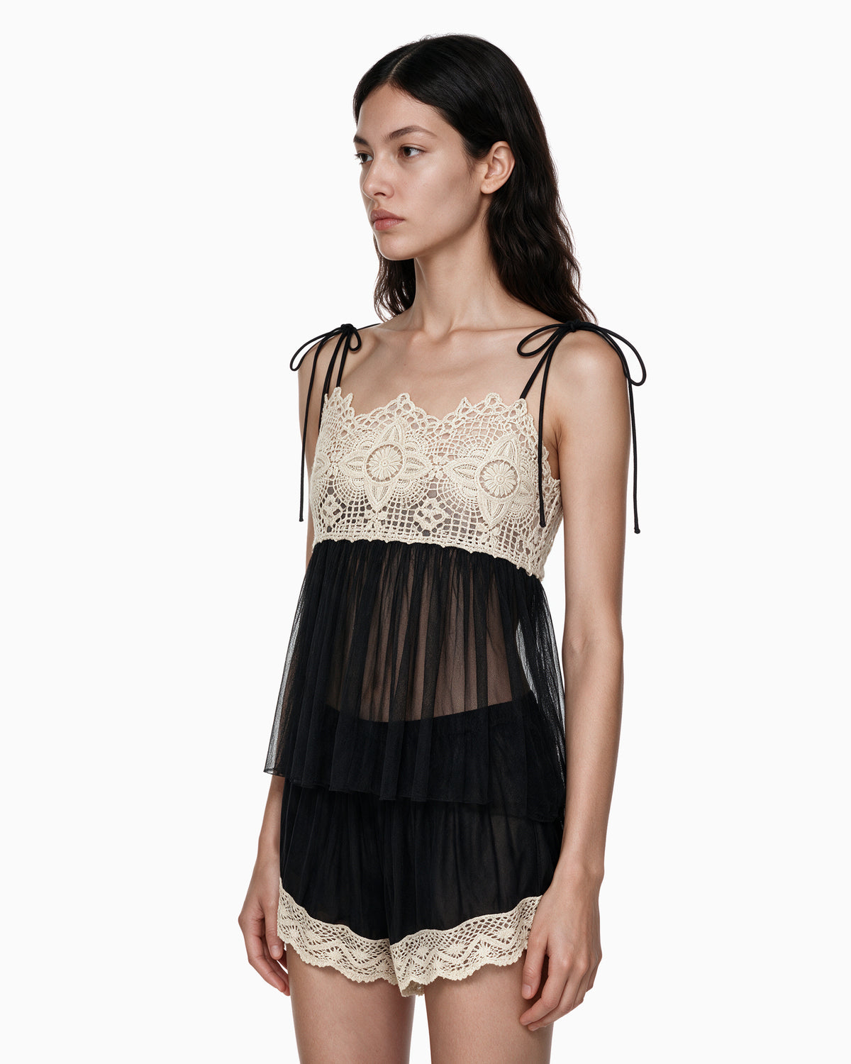 Modelo vestindo Mini Short Tule Com Renda preto, com cós elástico e acabamento em renda bege, vista lateral