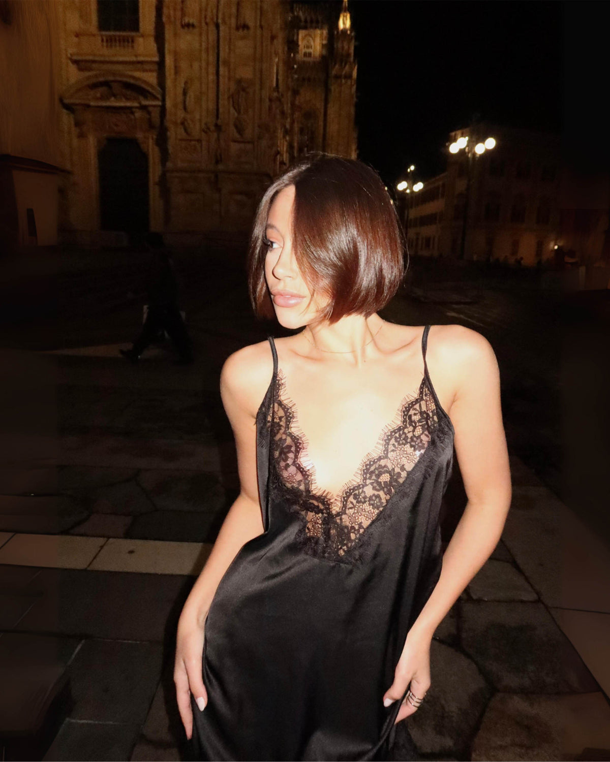 Detalhe do decote V profundo em renda do Vestido Affair preto acetinado com alças finas na modelo