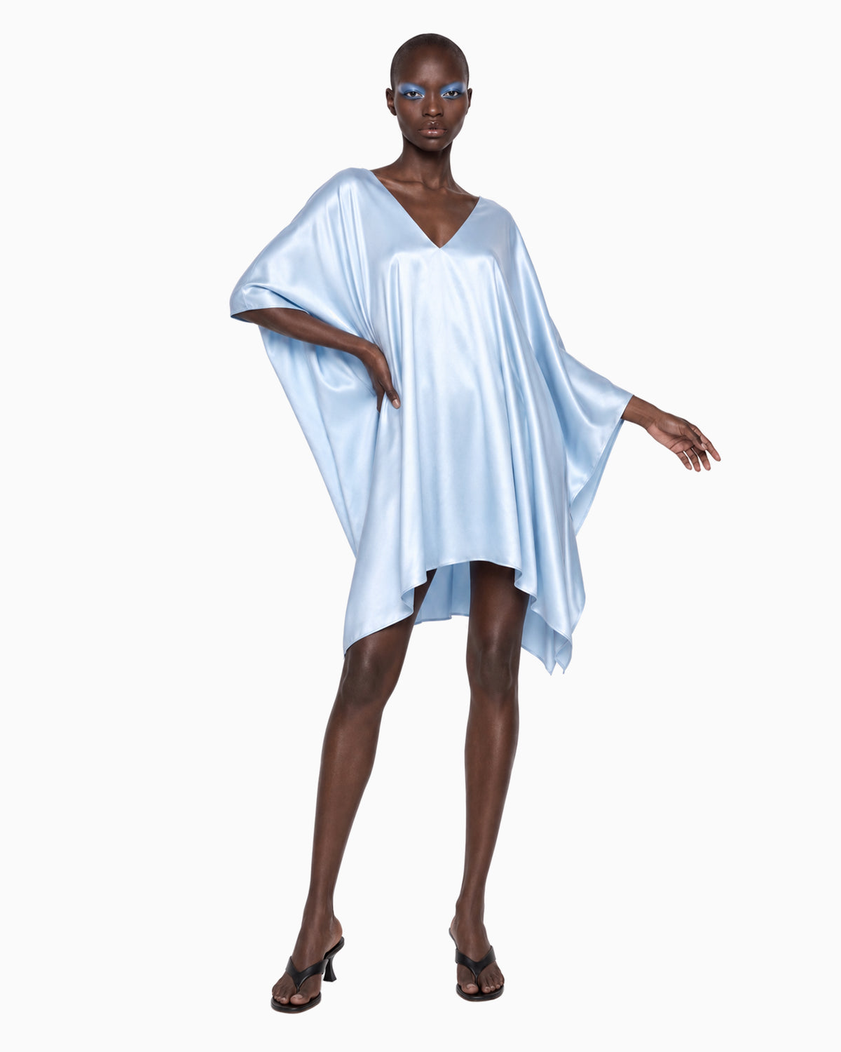 Modelo de frente com Vestido Curto Manga Morcego Ivo azul claro, braço erguido mostrando a manga ampla de cetim