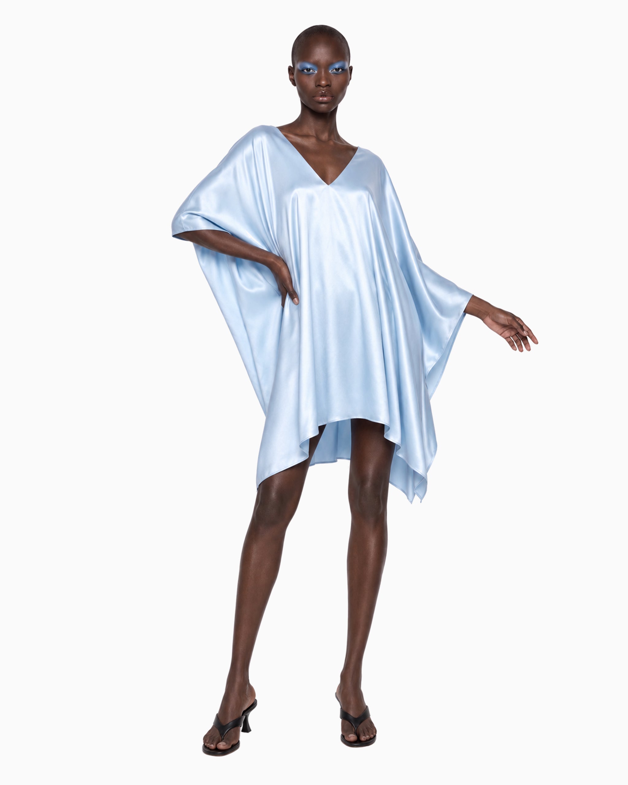 Modelo de frente com Vestido Curto Manga Morcego Ivo azul claro, braço erguido mostrando a manga ampla de cetim