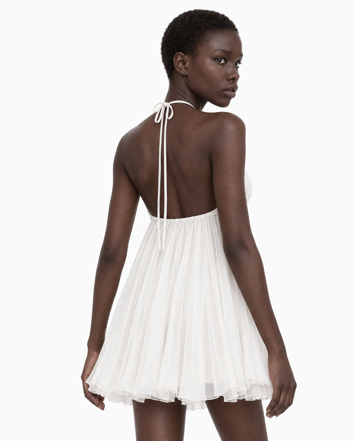 Modelo vestindo Vestido Curto Plissado branco com decote profundo, vista de costas