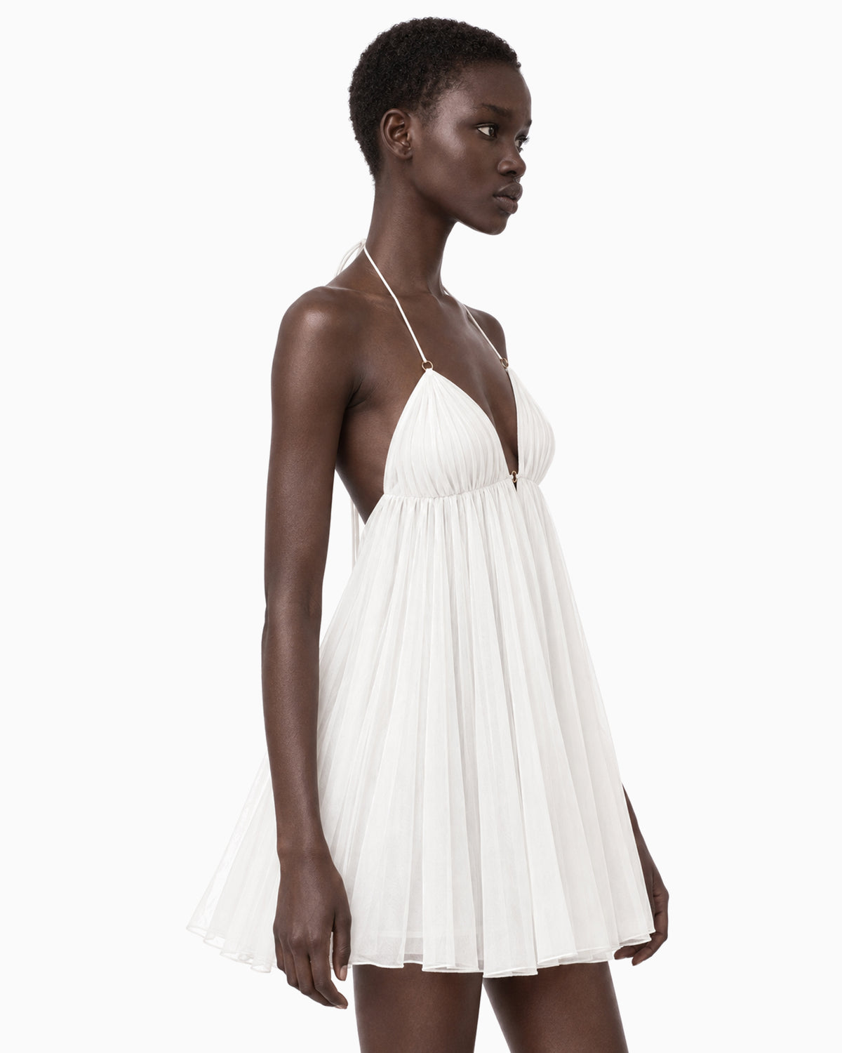 Modelo vestindo Vestido Curto Plissado branco com decote profundo, vista lateral