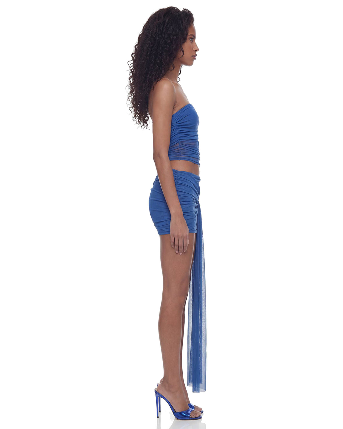 Vista lateral do Vestido Curto Transpasses Tule Hexa azul na modelo, caimento justo e faixa de tule descendo pela lateral