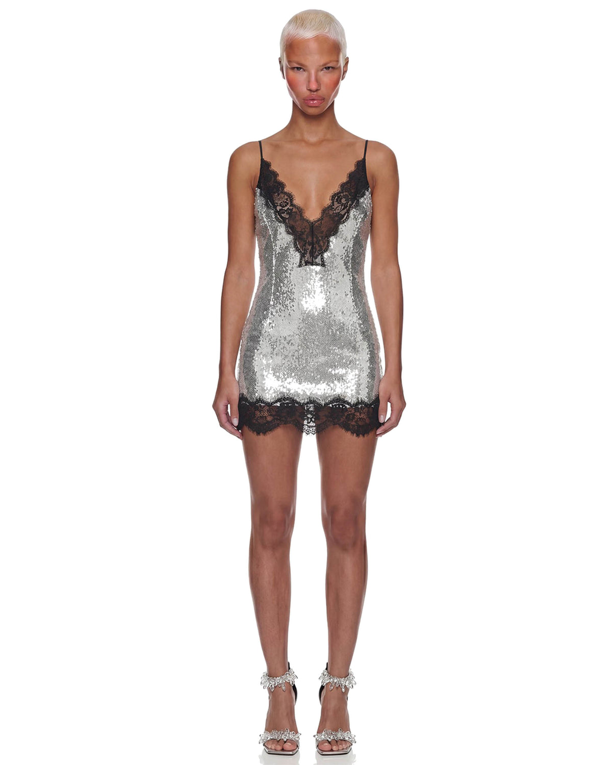 Modelo de frente com Vestido Decote Renda Paetê Aura prateado curto de paetês, decote em V de renda preta e alças finas